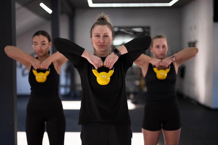 Three women in black outfits performing a coordinated dance move indoors.