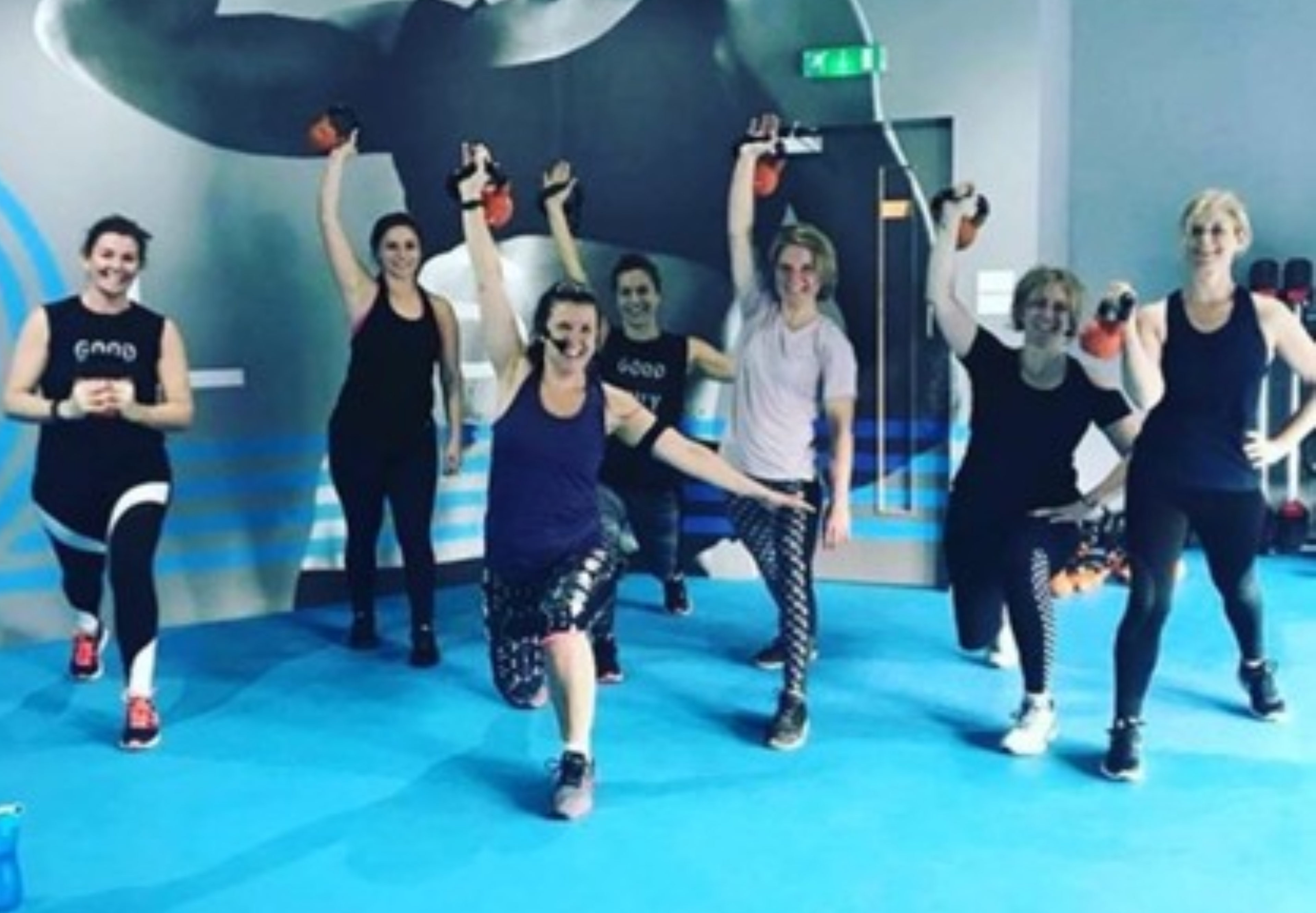Group of people posing with raised arms in a gym or dance studio.