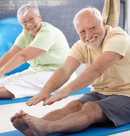 Two elderly people stretching on yoga mats indoors.