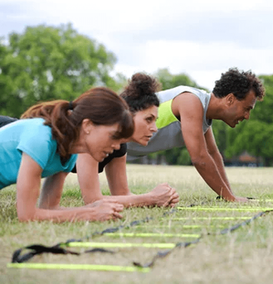 Three people doing plank exercises outdoors on mats.